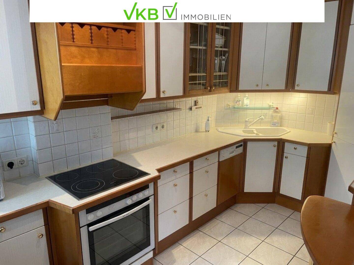 Funktionale Küche mit Holzschränken, weißen Fronten, Fliesenboden und integrierten Geräten.