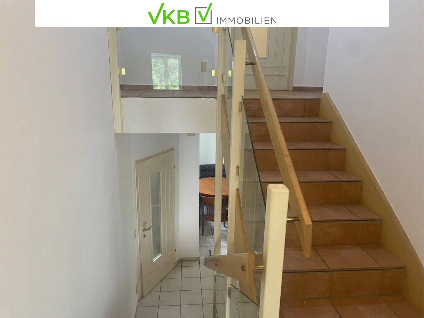 Treppenhaus mit moderner Glasbrüstung und Fliesenstufen, das die Etagen verbindet.