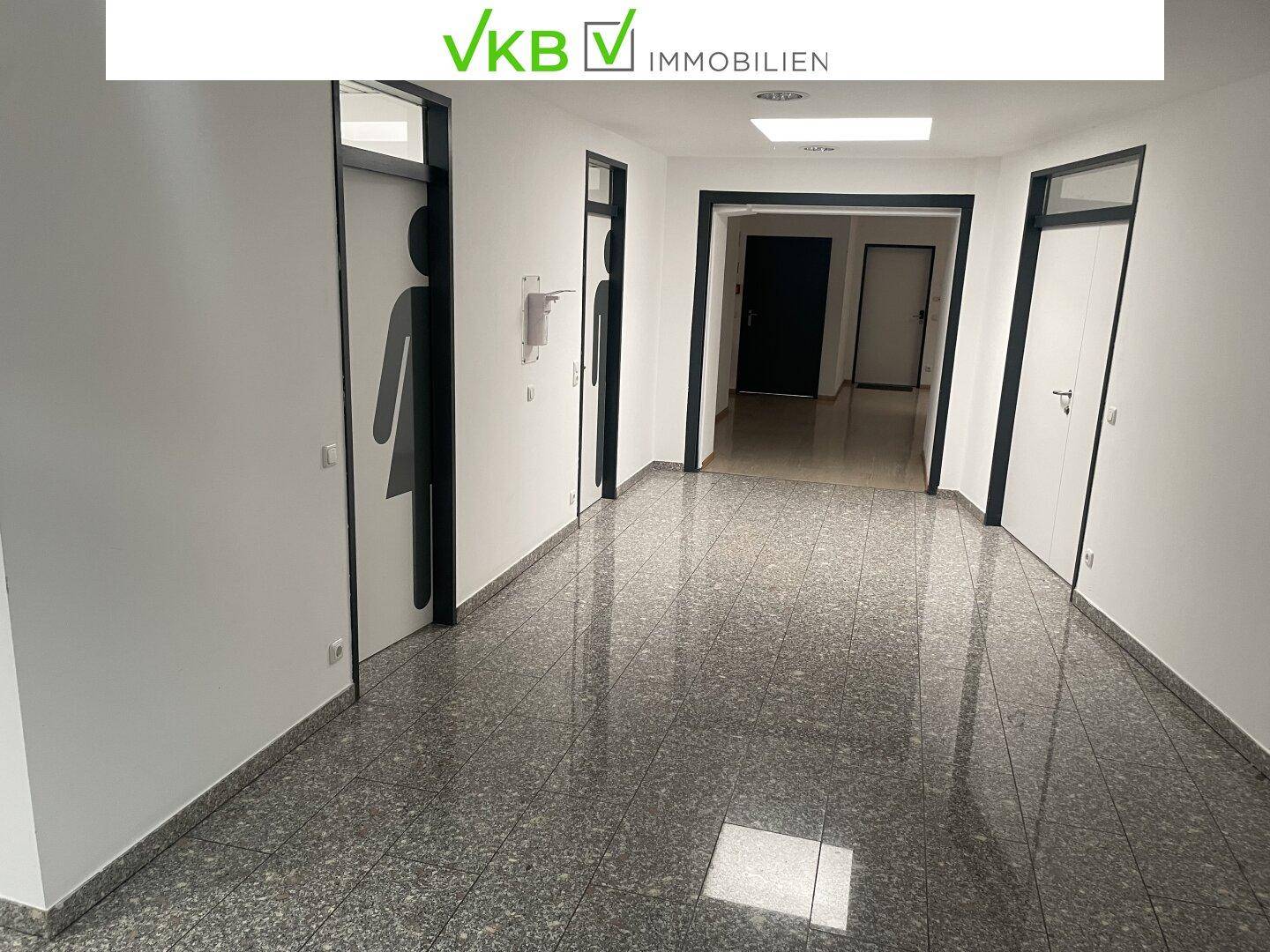 Langer Flur mit Steinfußboden und Türen zu verschiedenen Räumen, inklusive Toilettenbereichen.