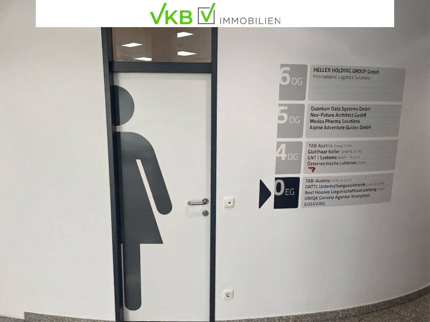 Flur mit Wegweiser zu den Büros und einer Tür zum Damen-WC, alles in einem modernen Design.