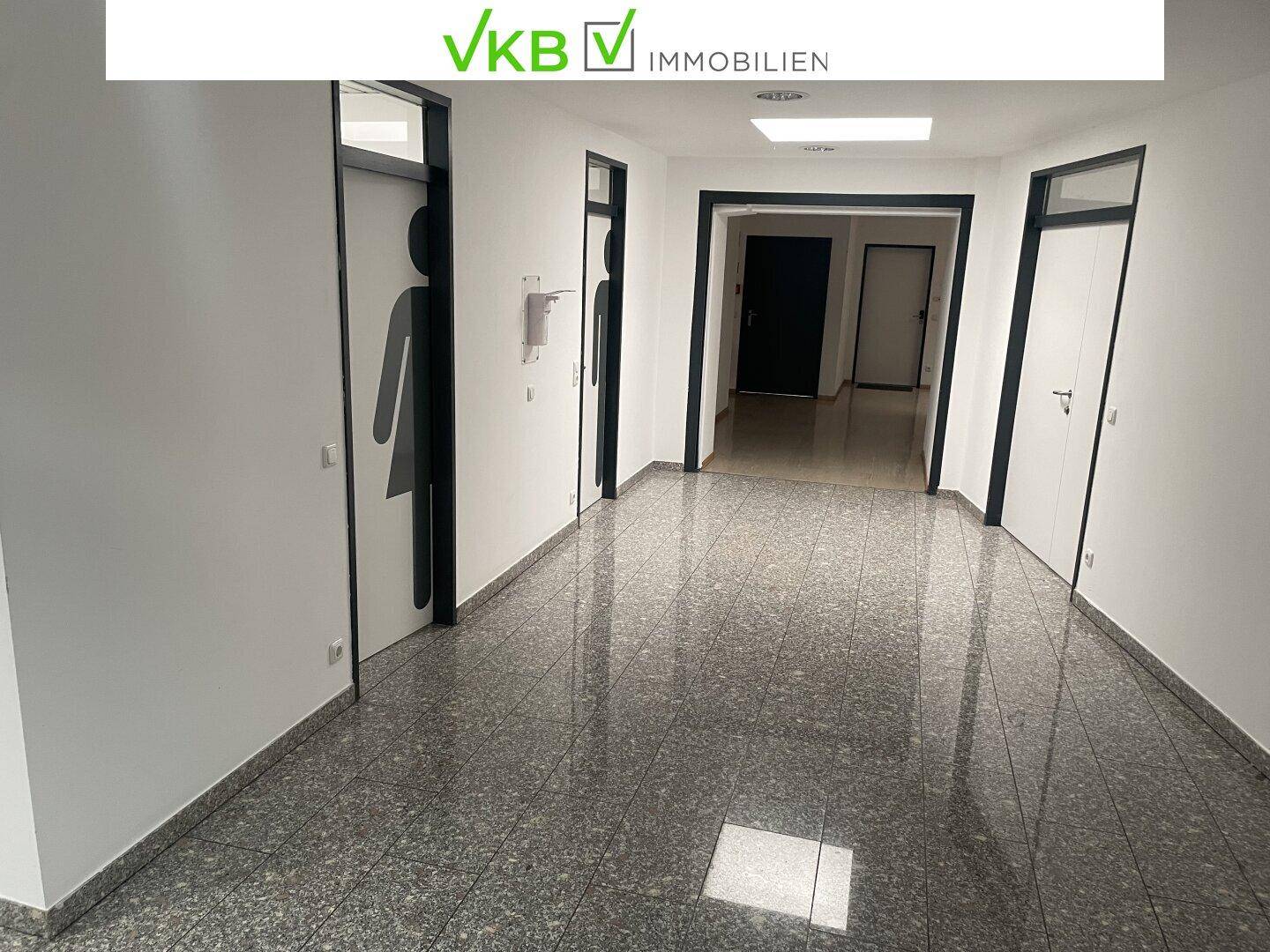 Langer Flur mit mehreren Türen, darunter Toiletten, und glänzendem Steinboden.