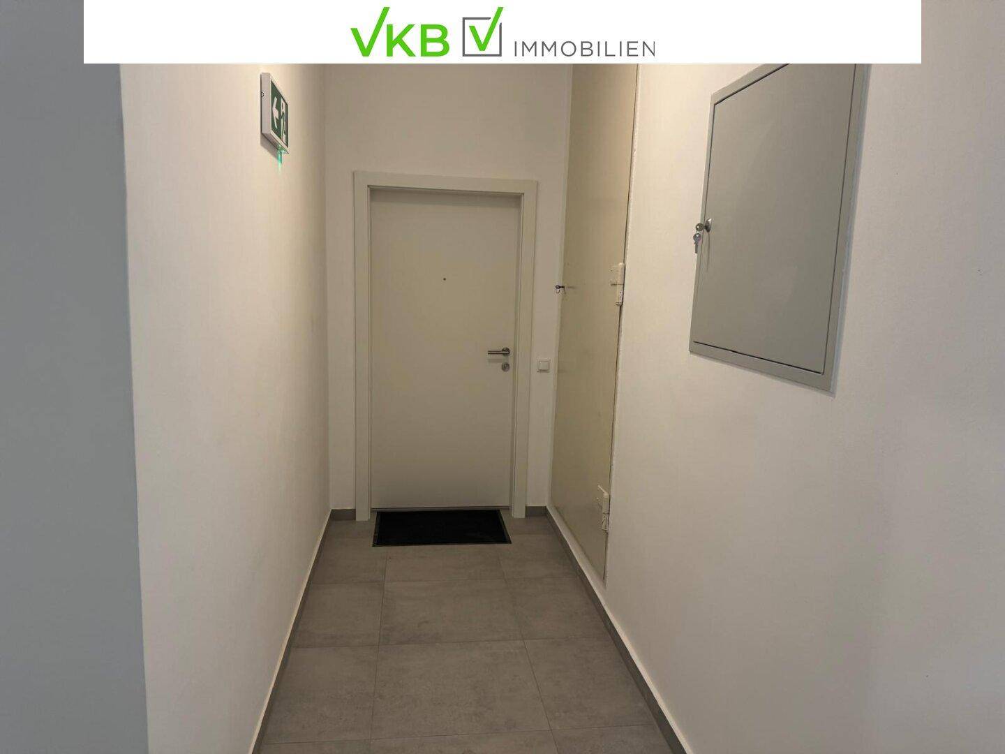 Heller Flur mit Fliesenboden und einer Eingangstür, die zu einer Wohneinheit führt.