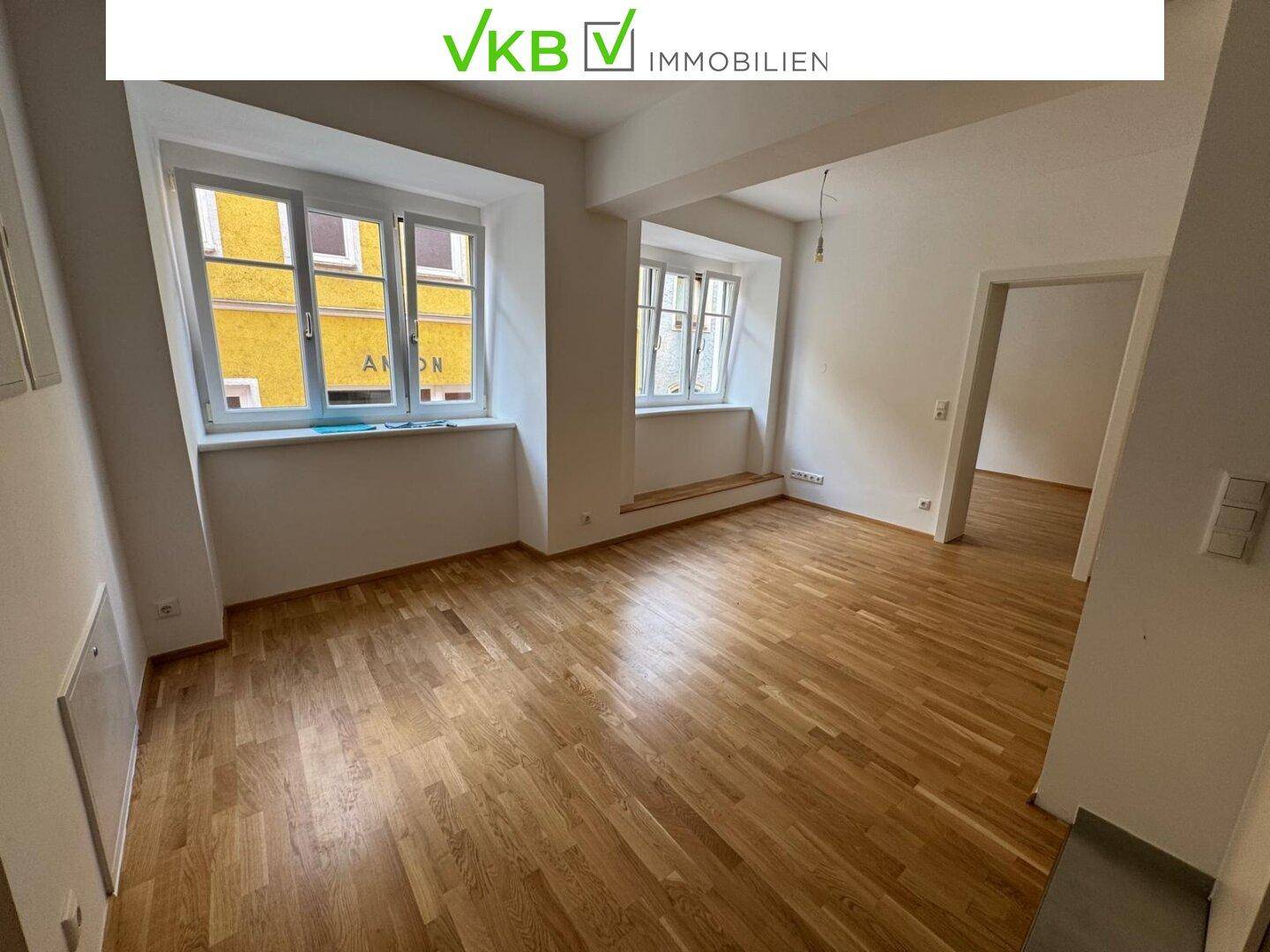 Heller Wohnraum mit Holzboden und mehreren Fenstern, die einen Blick nach draußen ermöglichen.