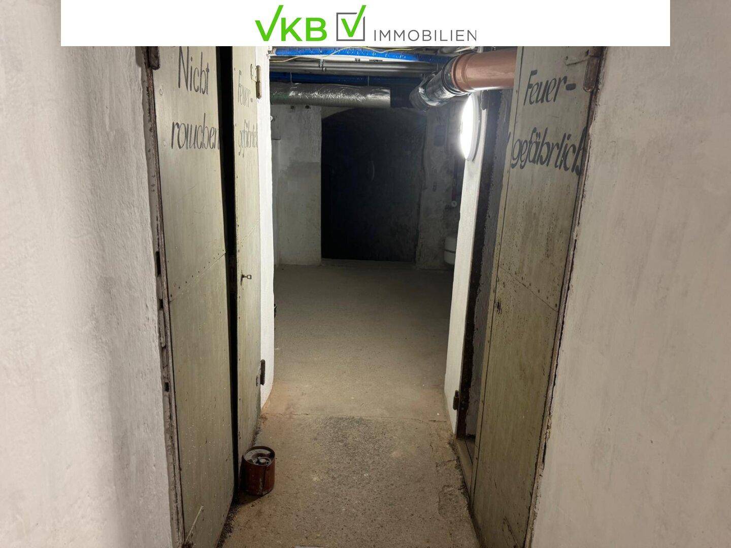 Dunkler Kellerflur mit alten Holztüren und Hinweisschildern, die auf Rauchverbot hinweisen.