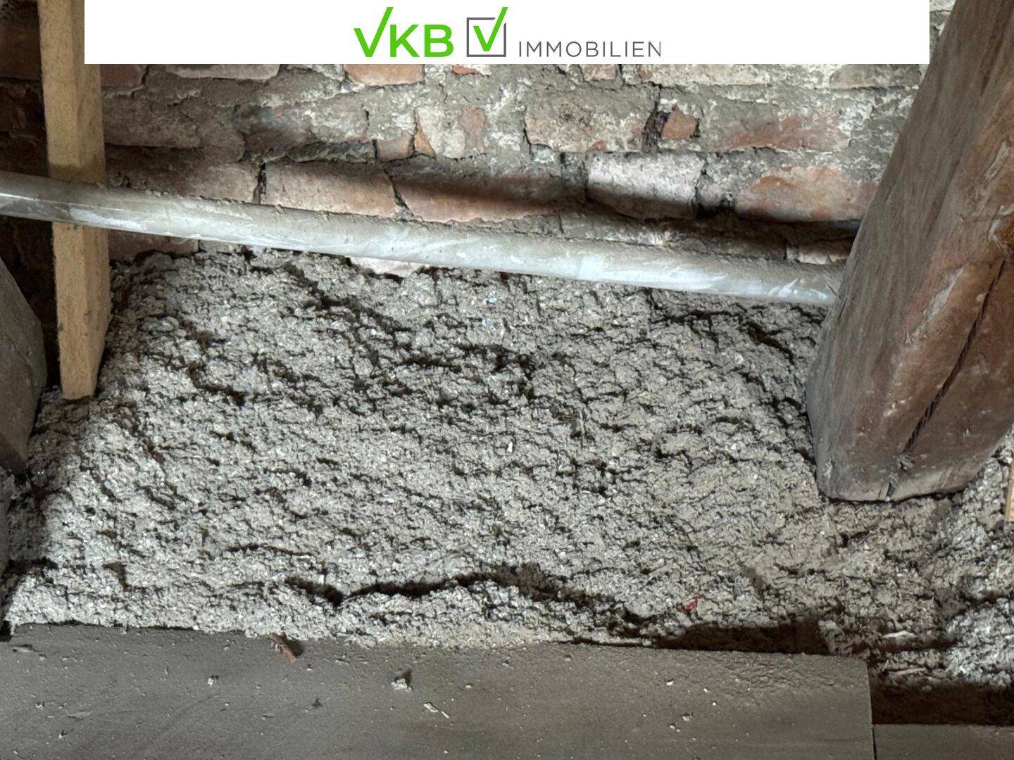 Nahaufnahme von Dämmmaterial zwischen Holzbalken und altem Mauerwerk im Dachbereich des Gebäudes.