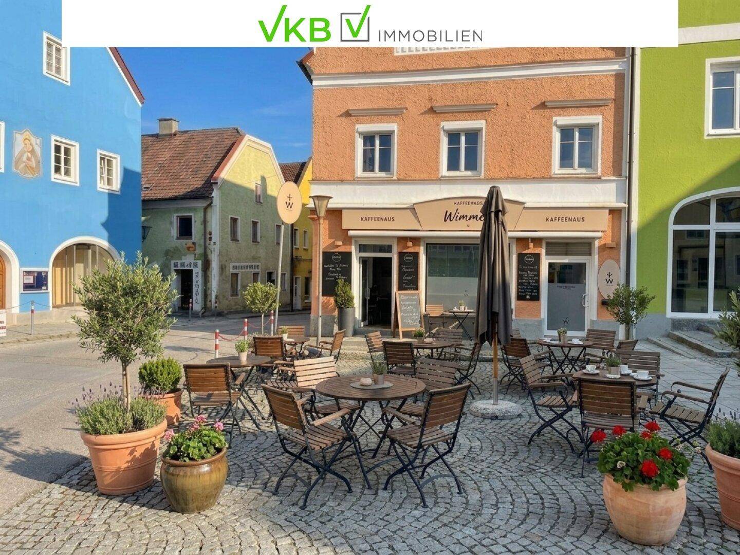 Malerischer Außenbereich mit Tischen und Stühlen vor einem farbenfrohen Gebäude in einer historischen Gasse.