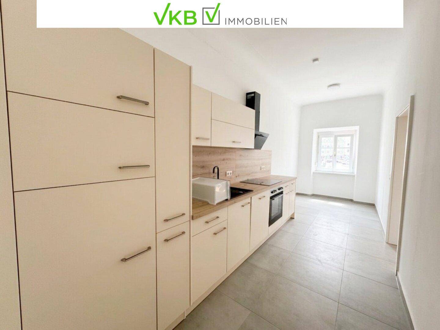 Moderne Einbauküche mit hellen Schränken, Holz-Arbeitsplatte und integrierten Geräten.