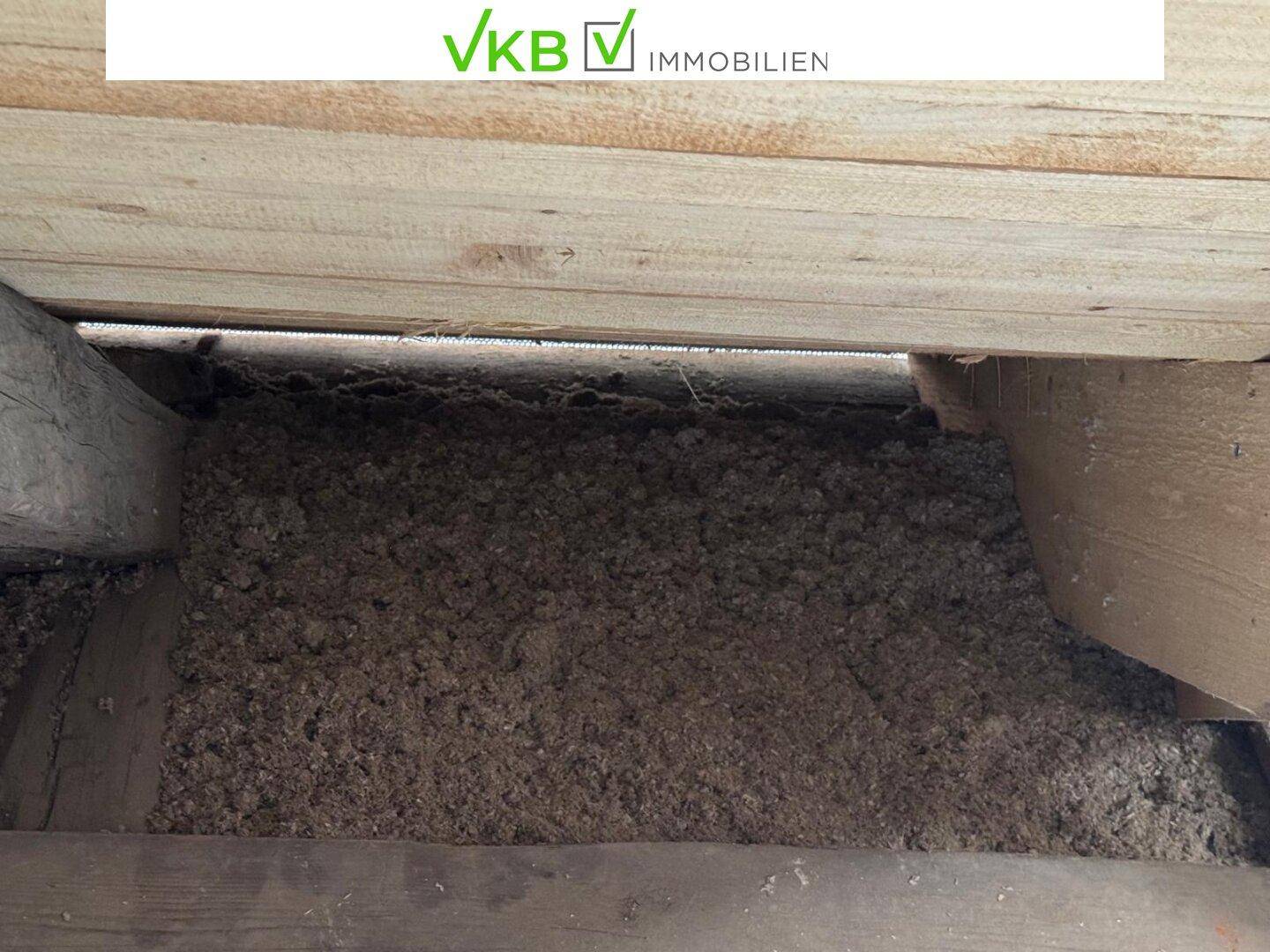 Dämmung aus losem Material zwischen Holzbrettern und Balken im Dachstuhl, zeigt den Bauzustand.