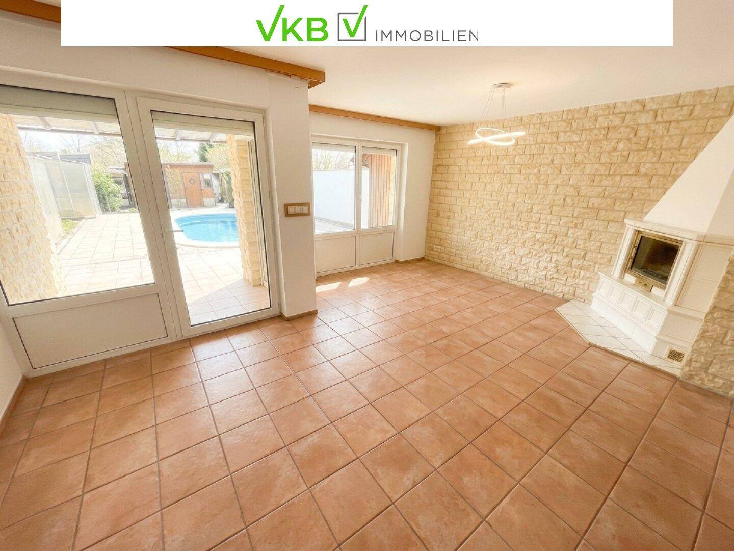 Helles Wohnzimmer mit Kamin, Fliesenboden und direktem Zugang zum Garten und Poolbereich.