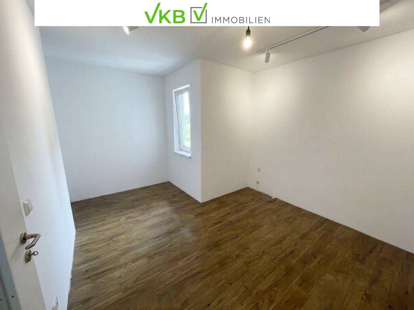 Leeres Zimmer mit Laminatboden und einem kleinen Fenster, bereit zur individuellen Gestaltung.