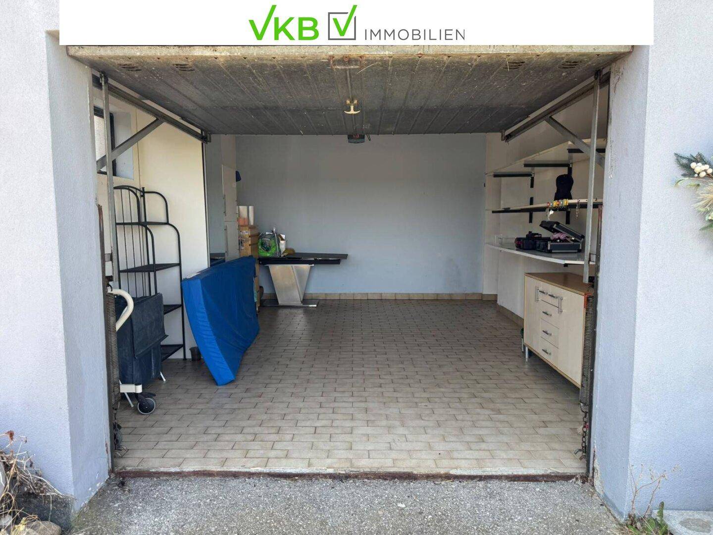 Geräumige Einzelgarage mit gefliestem Boden, Regalen und Stauraum für verschiedene Gegenstände.