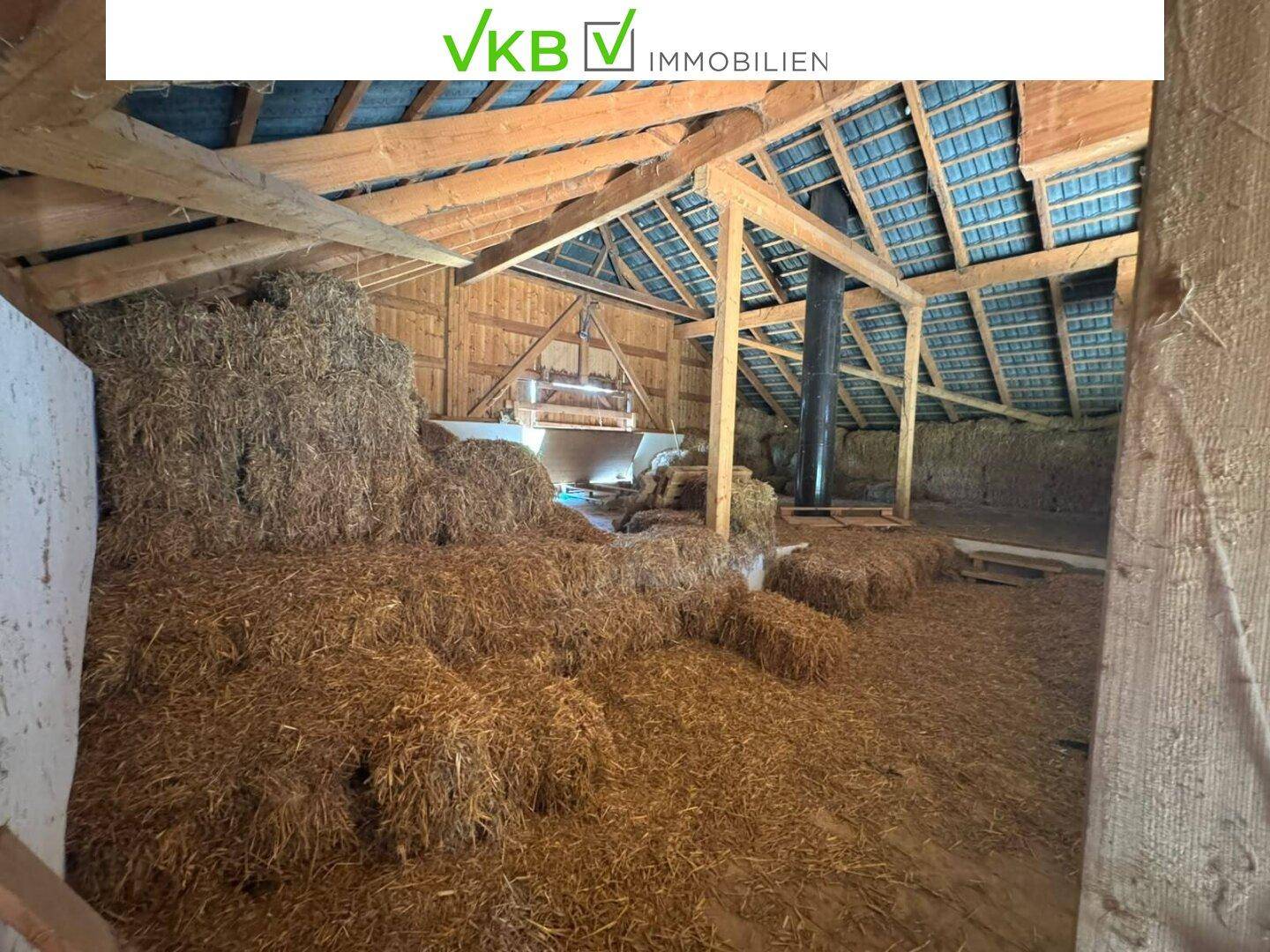 Scheuneninnenraum gefüllt mit Heuballen, unter einem sichtbaren Holzdachstuhl, für landwirtschaftliche Nutzung.
