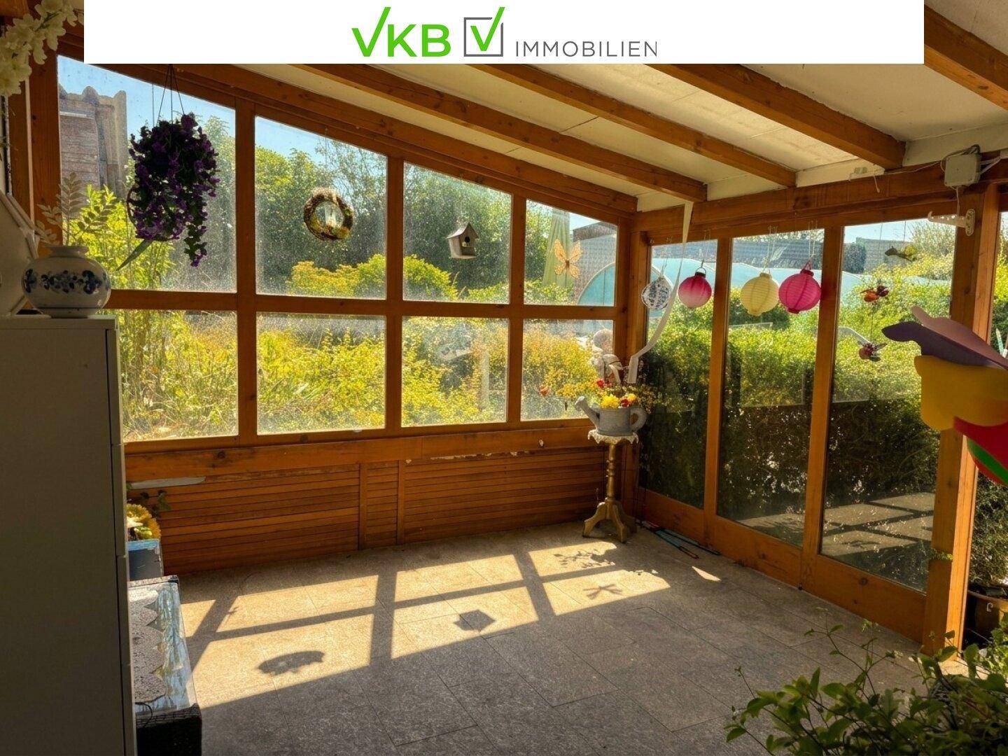 Heller Wintergarten mit großen Holzfenstern und Blick in den Garten, ideal für entspannte Stunden.