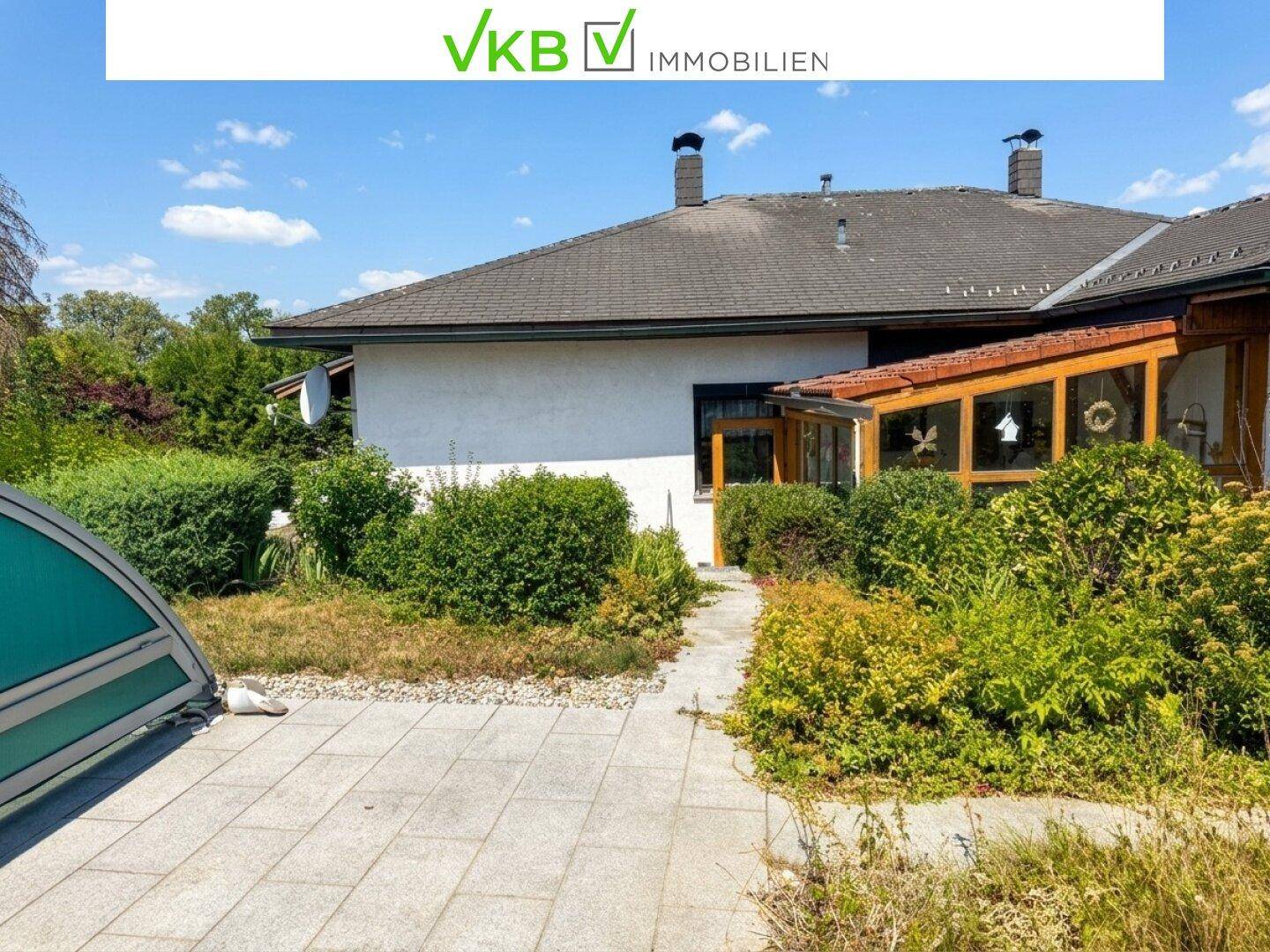 Seitenansicht des Hauses mit gepflastertem Bereich, Hecken und einem Wintergarten, der Pflege benötigt.