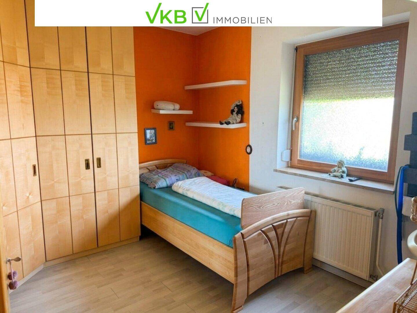 Kinderzimmer mit hellem Holzschrank, Einzelbett und orangefarbener Akzentwand, freundlich gestaltet.