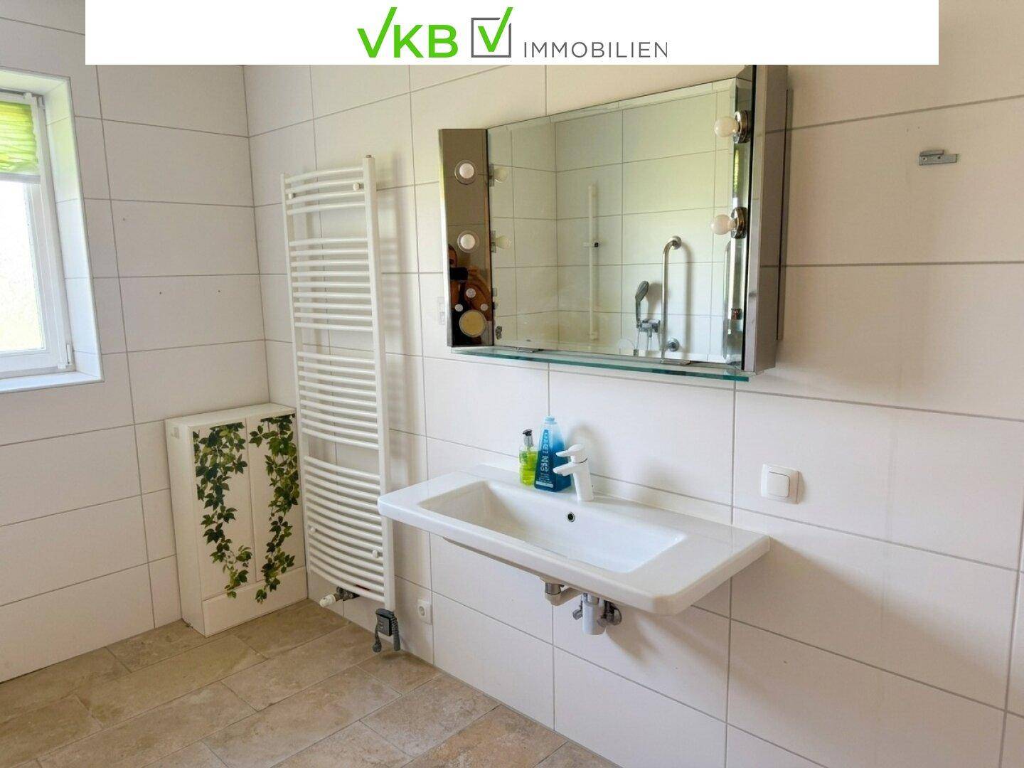 Helles Badezimmer mit Fliesenboden, Waschbecken und beheiztem Handtuchhalter, funktional und sauber.