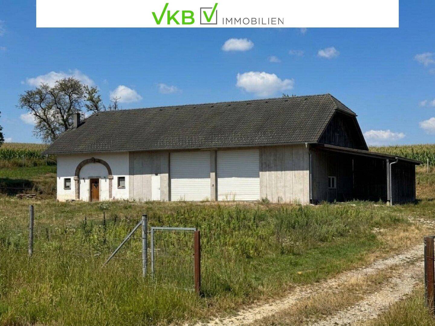 Großes landwirtschaftliches Gebäude mit traditionellem Dach, umgeben von weiten Feldern und Natur.