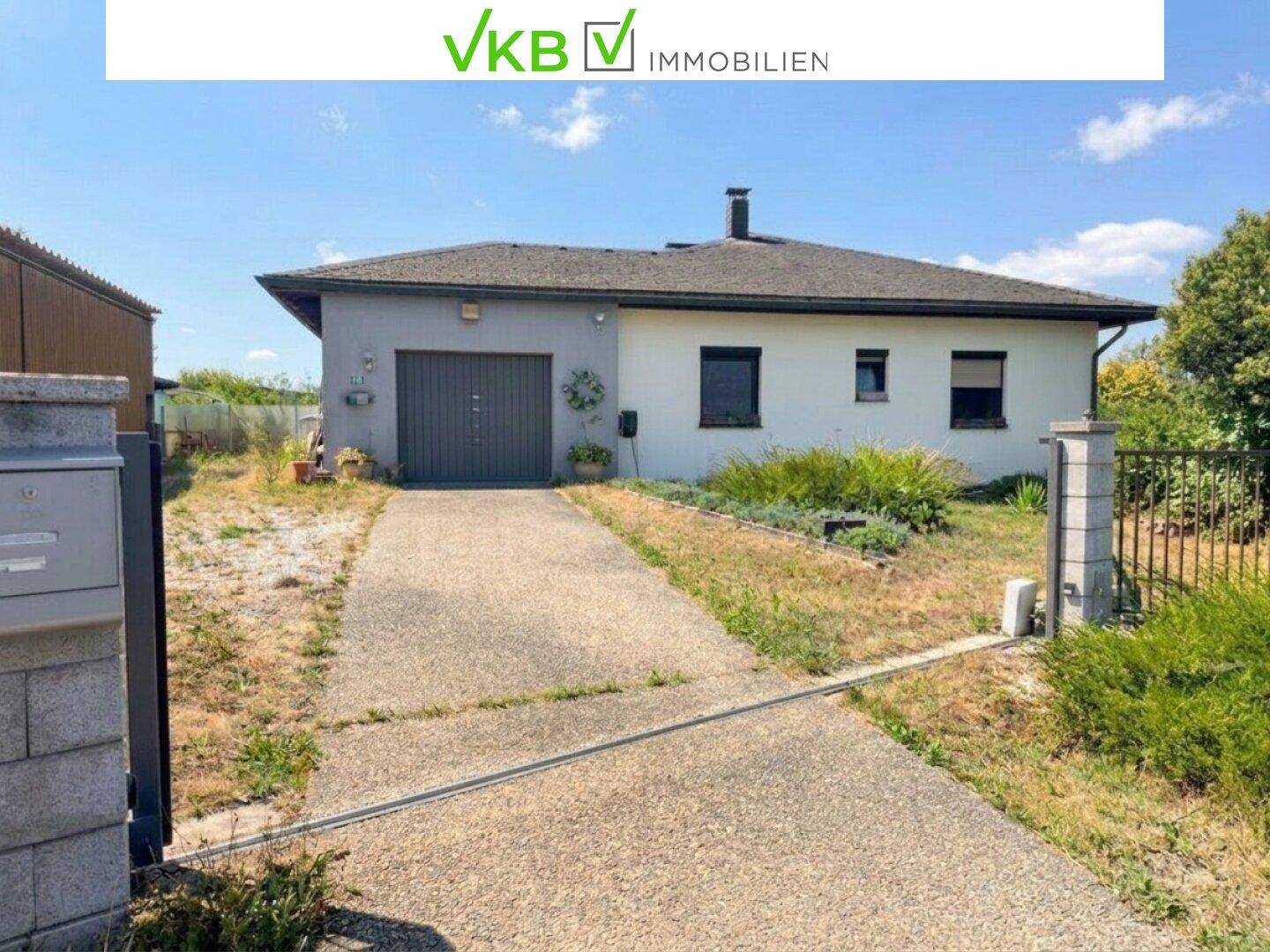 Vorderansicht eines Einfamilienhauses mit Zufahrt und ungepflegtem Vorgarten unter blauem Himmel.