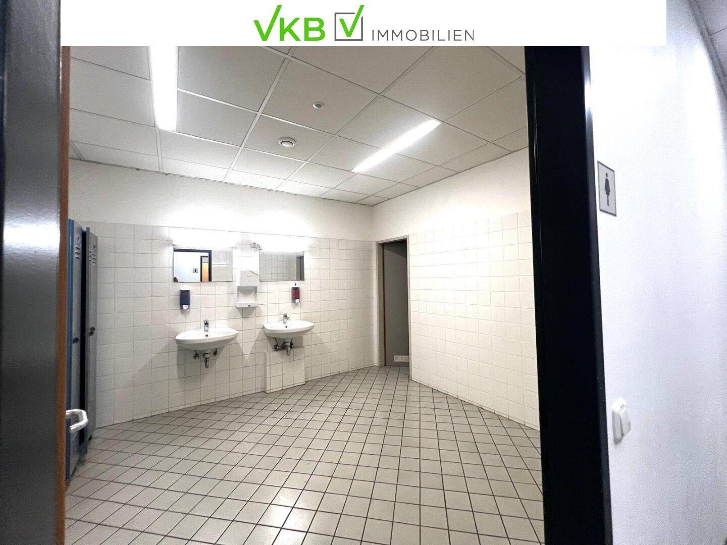 Umkleideraum mit Waschbecken, Spiegeln und Spinden, gefliest und gut beleuchtet, ideal für Mitarbeiter.