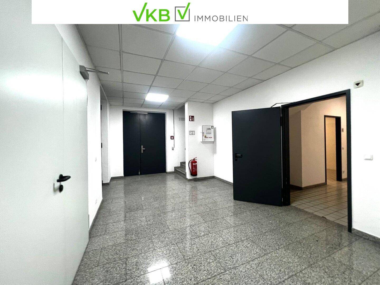 Geräumiger Flur mit Fliesenboden, mehreren Türen und einem Feuerlöscher, gut beleuchtet und funktional.