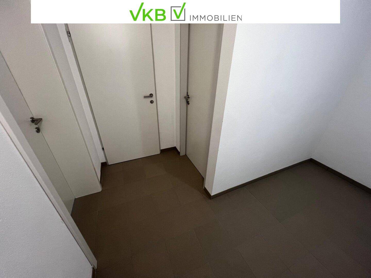 Leerer Flurbereich mit mehreren weißen Türen und dunklem Fliesenboden.