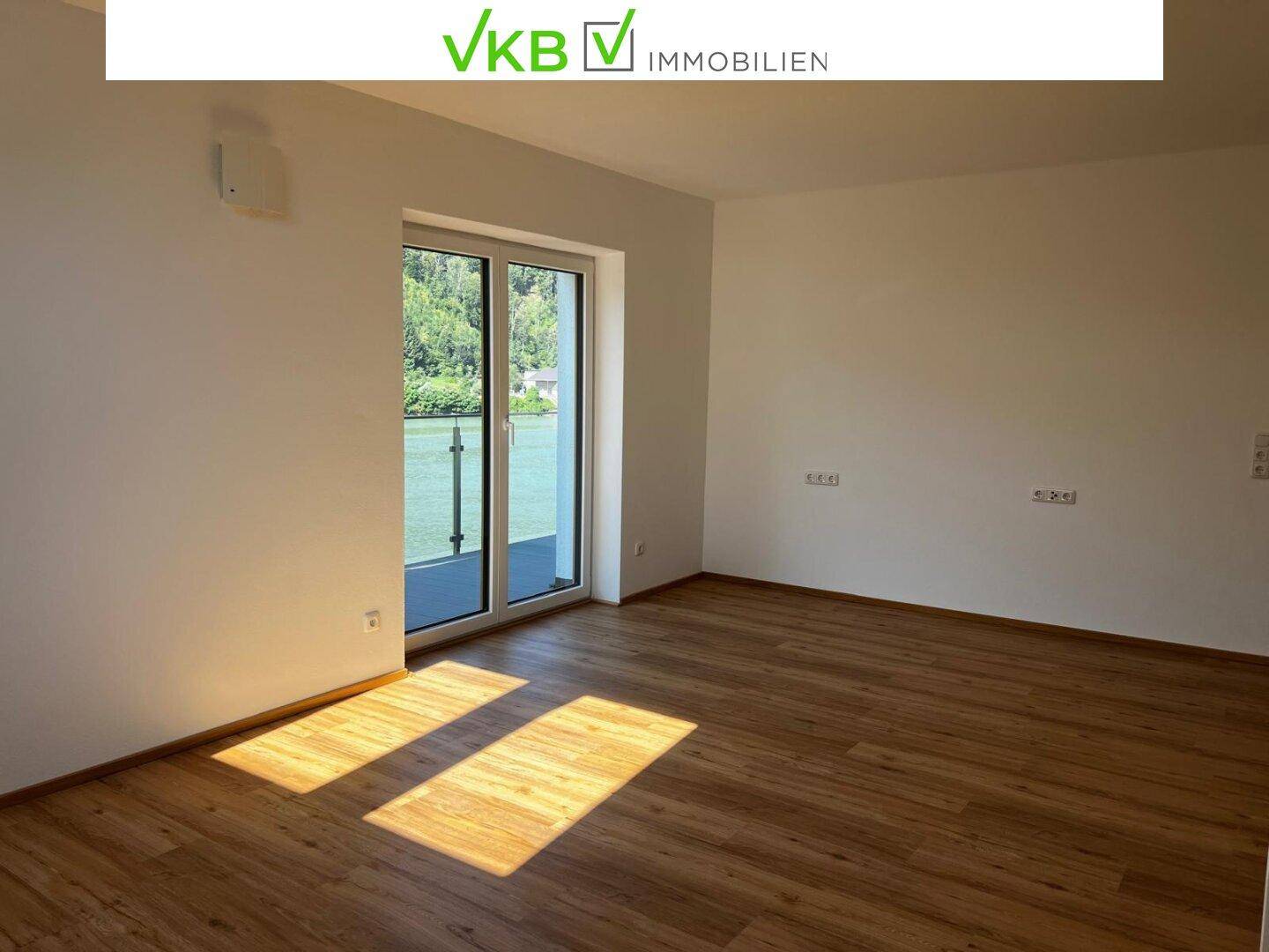 Lichtdurchfluteter Raum mit Balkonzugang und weitem Blick auf den Fluss und die Natur.