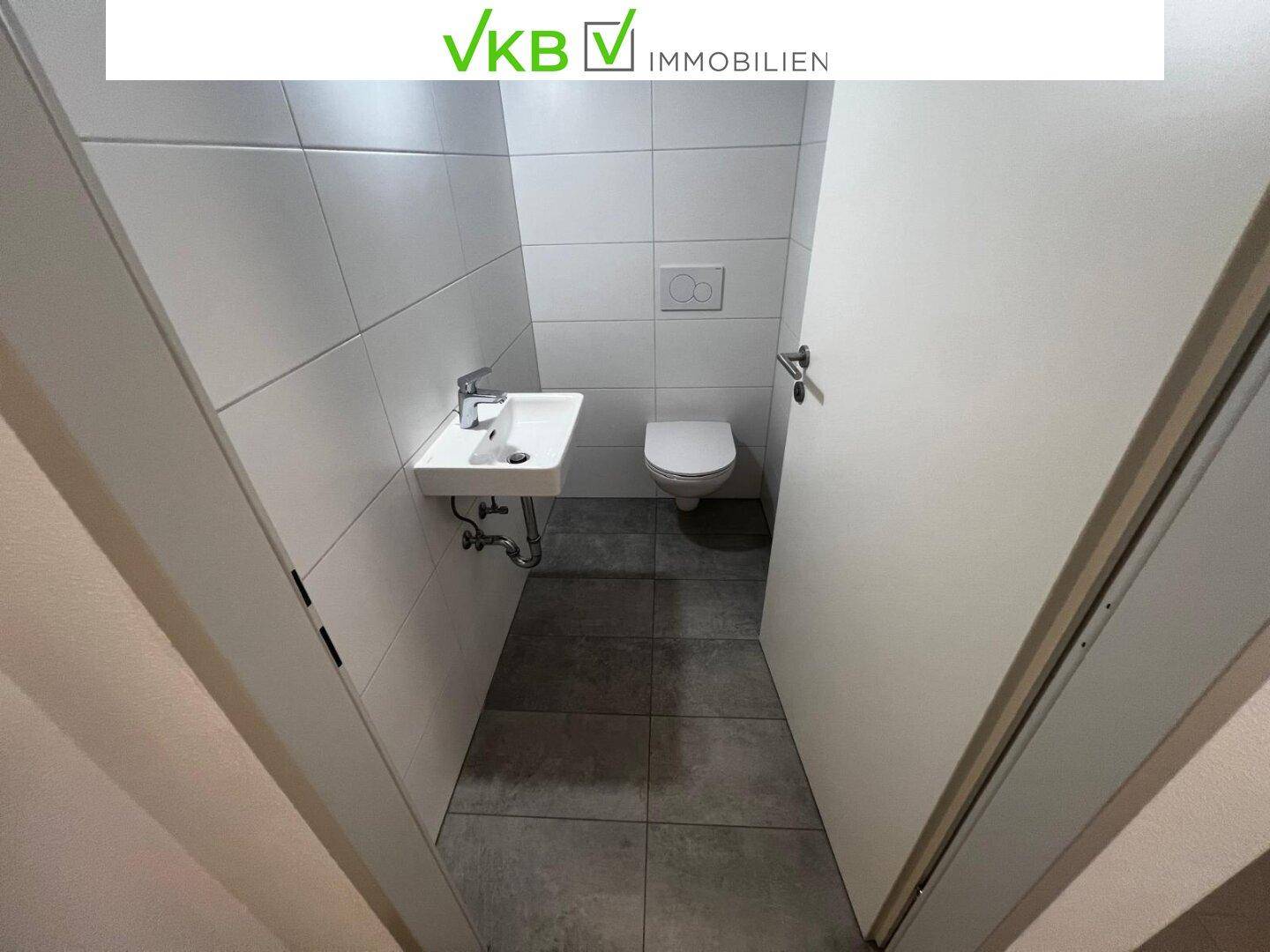 Modernes Gäste-WC mit Wand-WC, kleinem Waschbecken und hellen Fliesen.