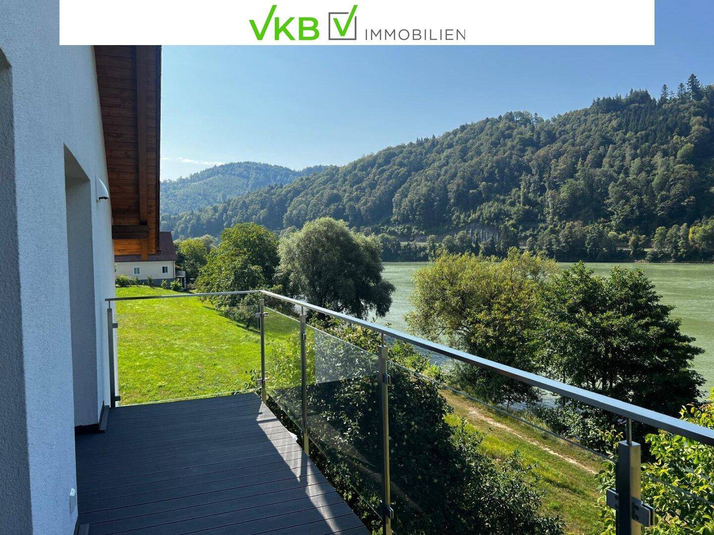 Geräumiger Balkon mit Glasgeländer und weitem Blick auf die grüne Umgebung und den Fluss.