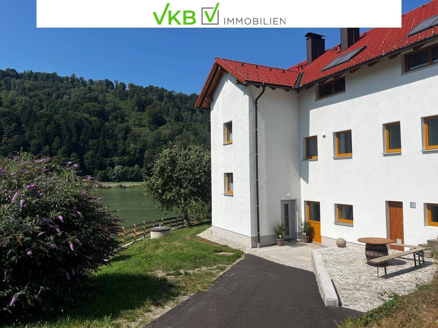 Weiß verputztes Gebäude mit rotem Ziegeldach und Blick auf den Fluss und die bewaldeten Hügel.