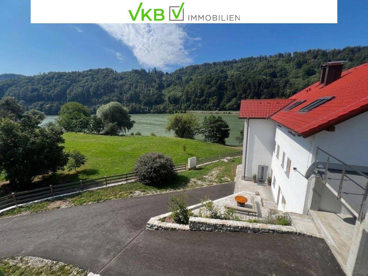 Ansicht des Gebäudes mit rotem Dach, umgeben von Grünflächen und Blick auf den Fluss.