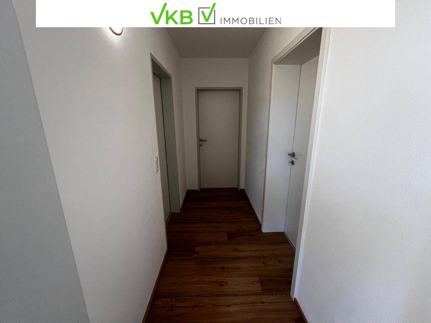 Langer Flur mit Laminatboden und weißen Wänden, der zu verschiedenen Räumen führt.