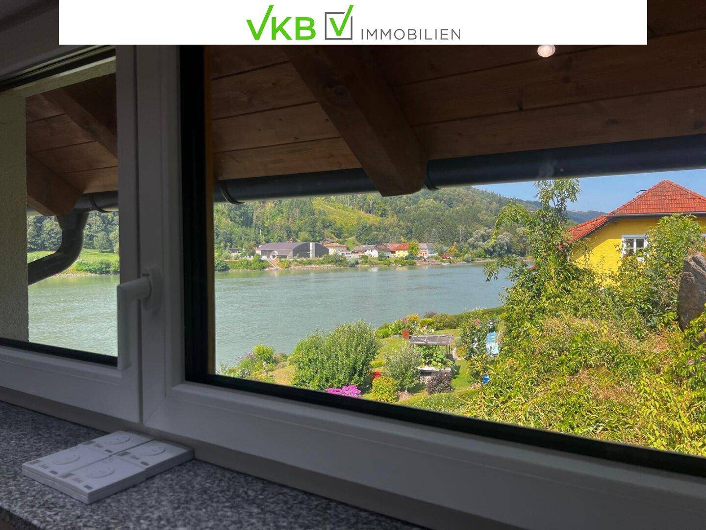 Fensterblick auf den Fluss, grüne Ufer und die gegenüberliegende Landschaft.