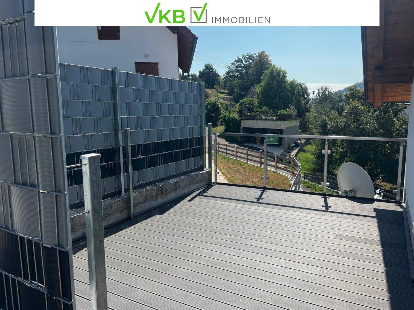 Moderner Balkon mit Holzdielenboden, Glasgeländer und weitem Blick auf die Umgebung.