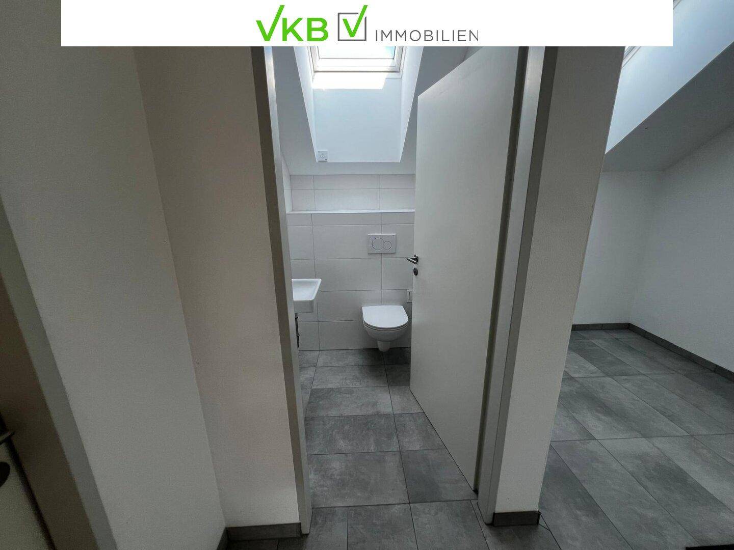 Modernes Gäste-WC mit wandhängendem WC, Waschbecken und Dachfenster für Tageslicht.