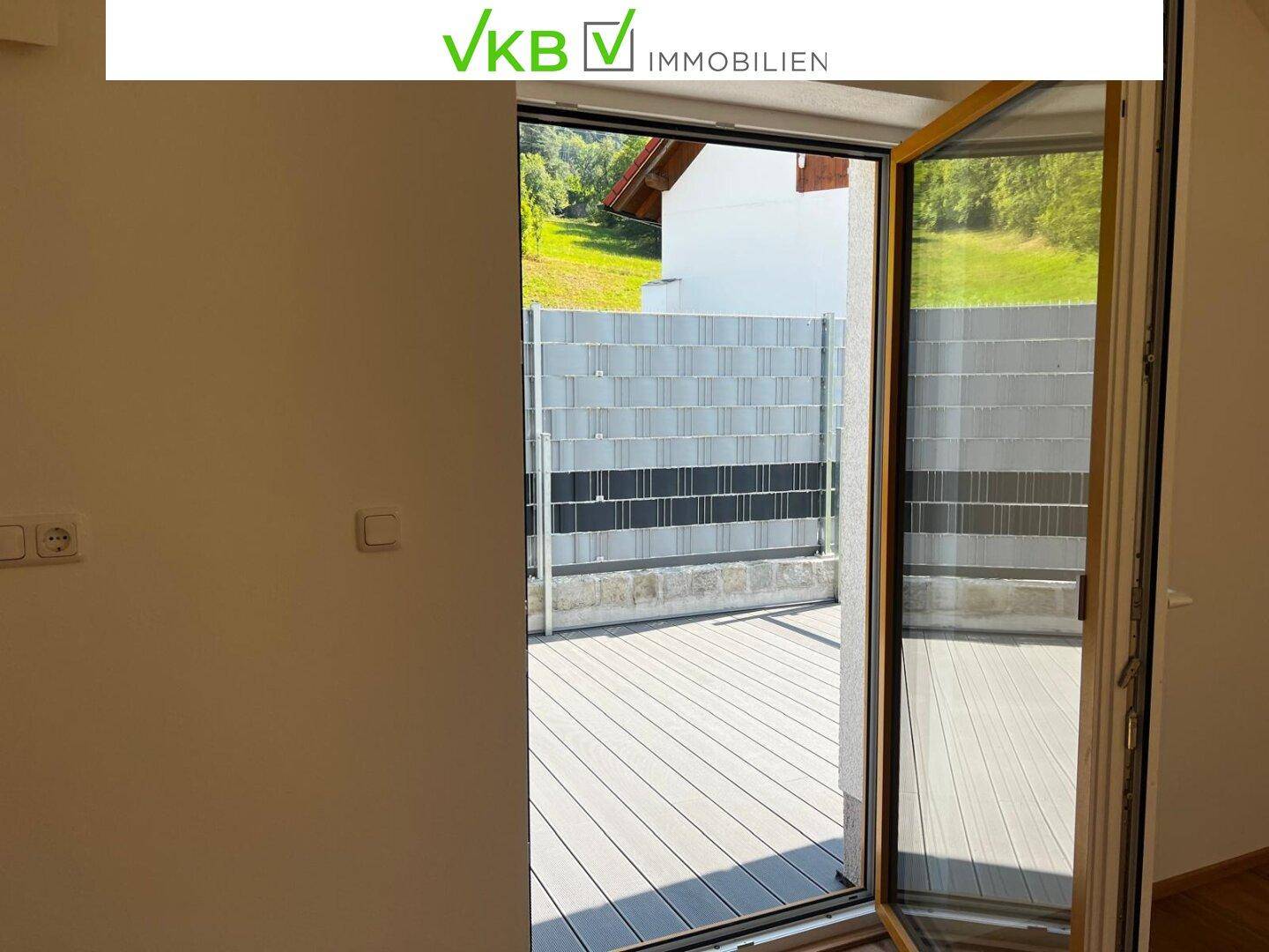 Zugang zu einem Balkon mit Holzdielenboden und Blick ins Grüne vom Innenraum.