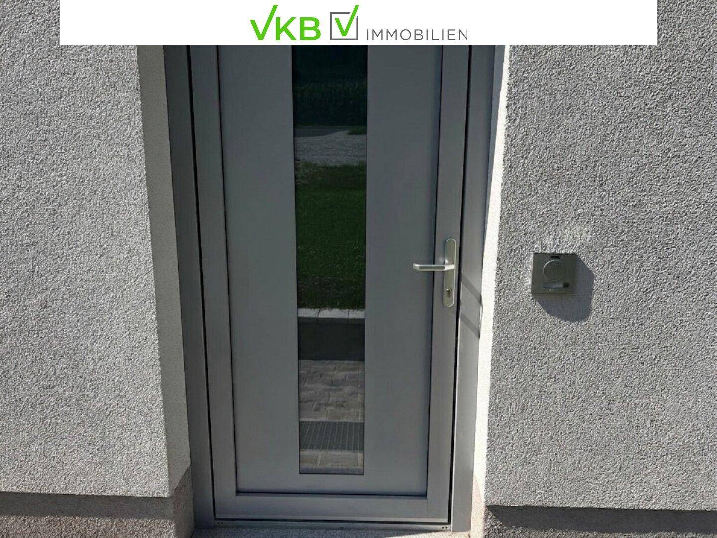 Nahaufnahme der modernen grauen Eingangstür mit Glaseinsatz und weißer Putzfassade.