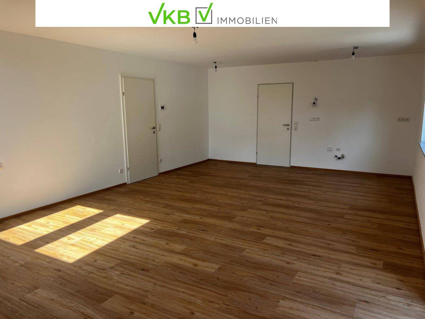 Heller Wohnraum mit Laminatboden, weißen Wänden und viel Tageslicht durch die Fenster.