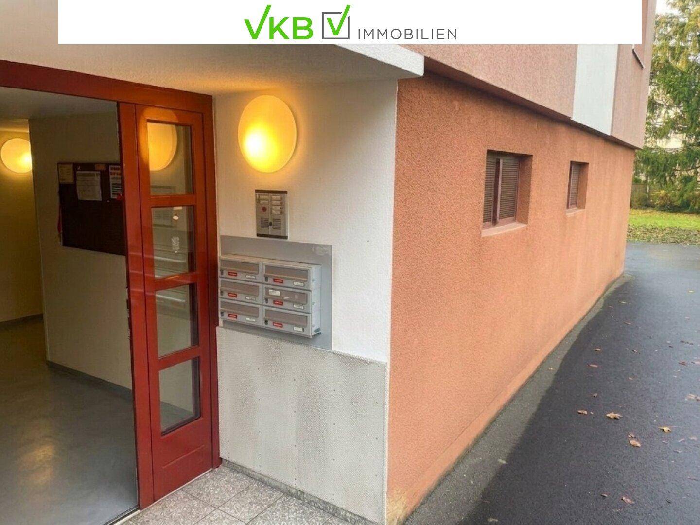 Eingangsbereich des Gebäudes mit Briefkästen, Gegensprechanlage und einer roten Eingangstür.