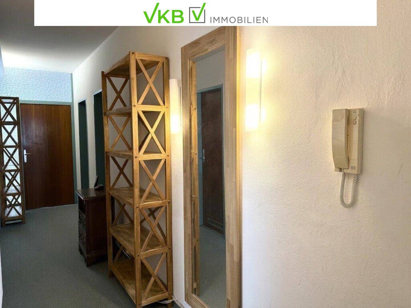 Heller Flur mit Holzregalen, einem großen Spiegel und einer Gegensprechanlage an der Wand.