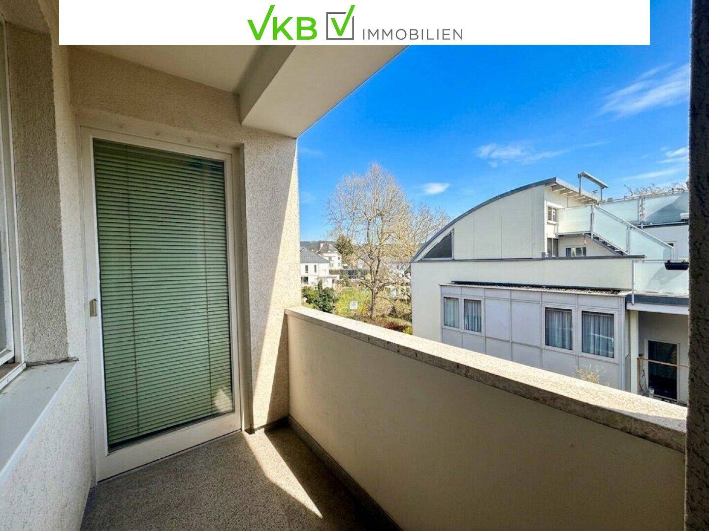 Heller Balkon mit Blick auf die umliegende Wohngegend und einen blühenden Baum im Frühling.