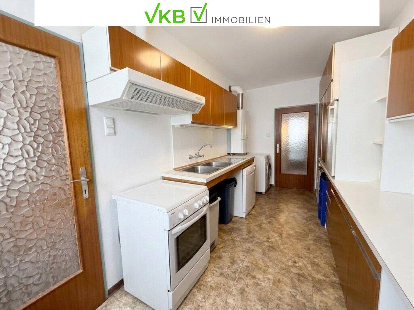Funktionale Küche mit älteren Holzschränken, Spüle und einem freistehenden Elektroherd.