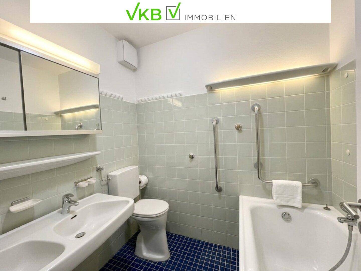 Badezimmer mit hellgrünen Fliesen, Badewanne, Waschbecken und einem Spiegelschrank.