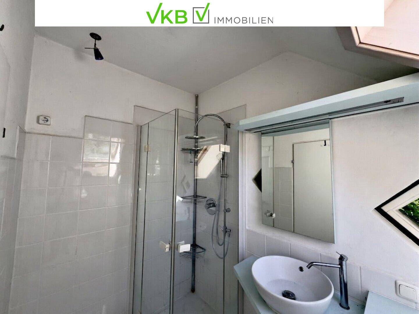 Badezimmer mit weiß gefliesten Wänden, Duschkabine und modernem Waschbecken unter einem Dachfenster.