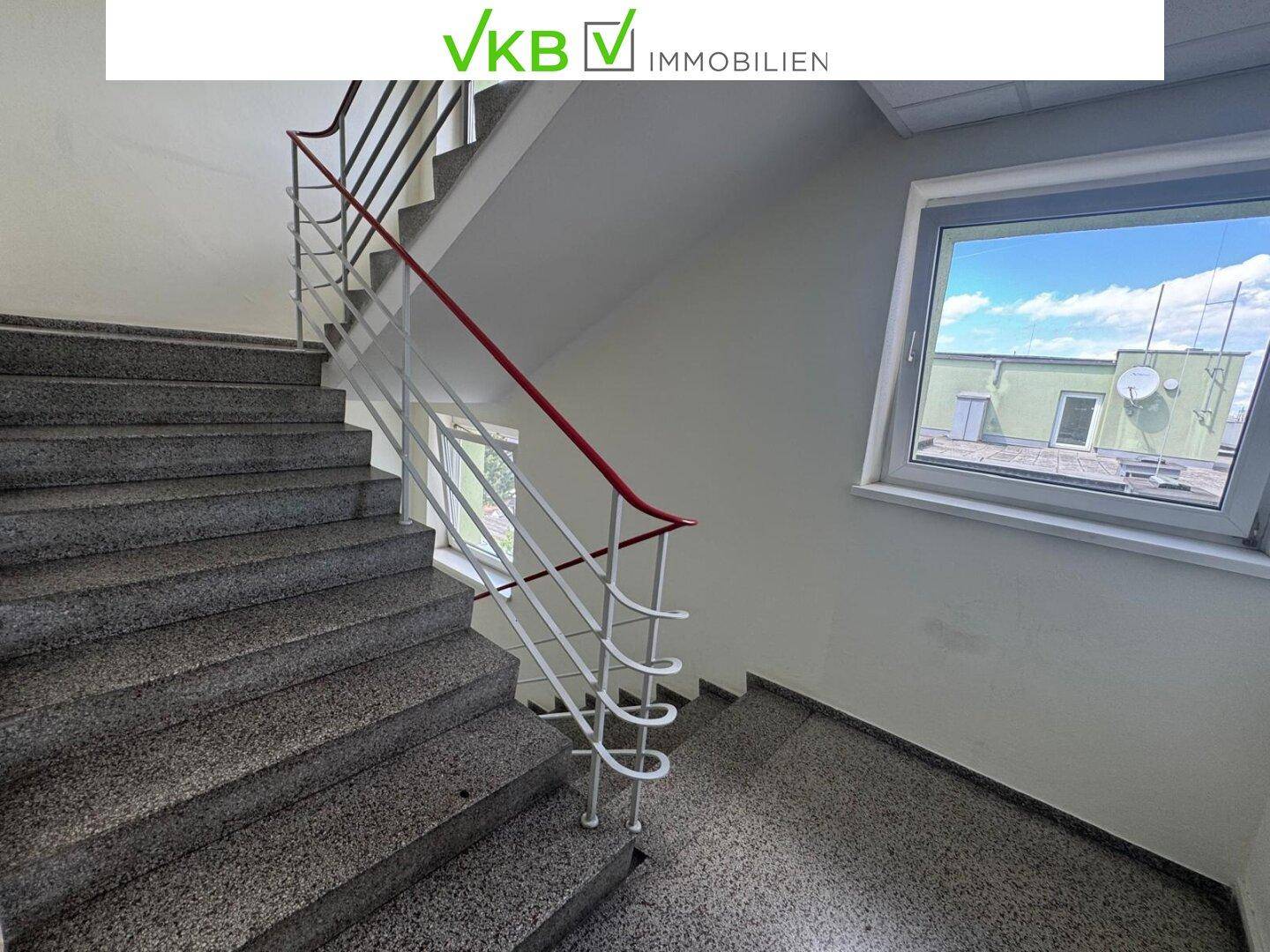 Treppenhaus mit Steinstufen und rotem Geländer, führt zu den oberen Etagen.