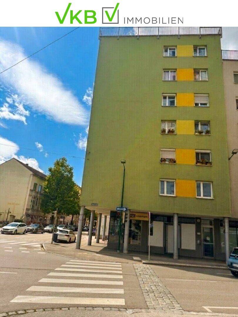 Mehrstöckiges Gebäude mit grüner und gelber Fassade an einer Straßenecke.