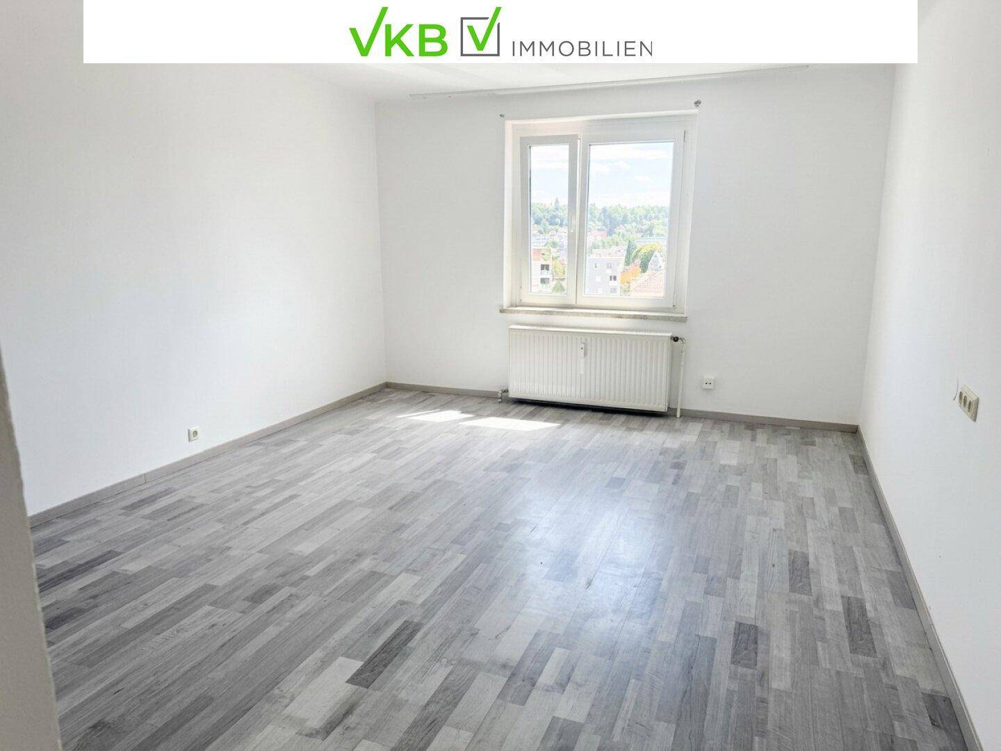 Helles Wohnzimmer mit grauem Laminatboden und großem Fenster, bereit zur individuellen Gestaltung.