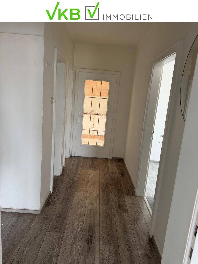 Heller Flur mit Laminatboden und einer Tür mit Glaseinsätzen, die Tageslicht hereinlässt.