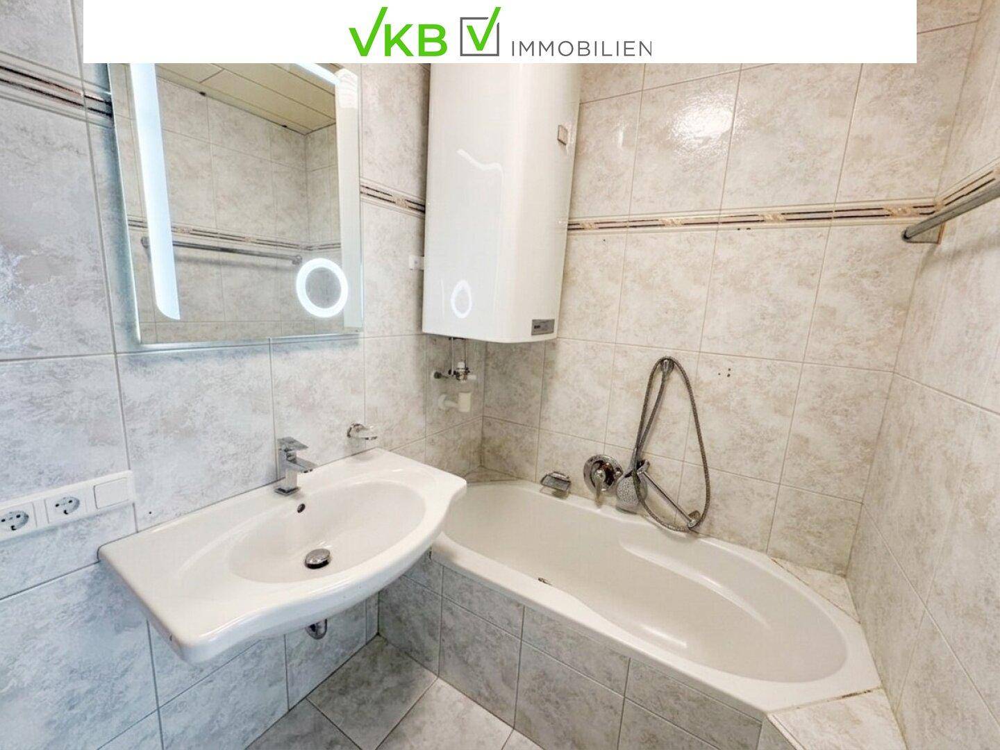 Gefliestes Badezimmer mit Badewanne, Waschbecken und beleuchtetem Spiegelschrank.