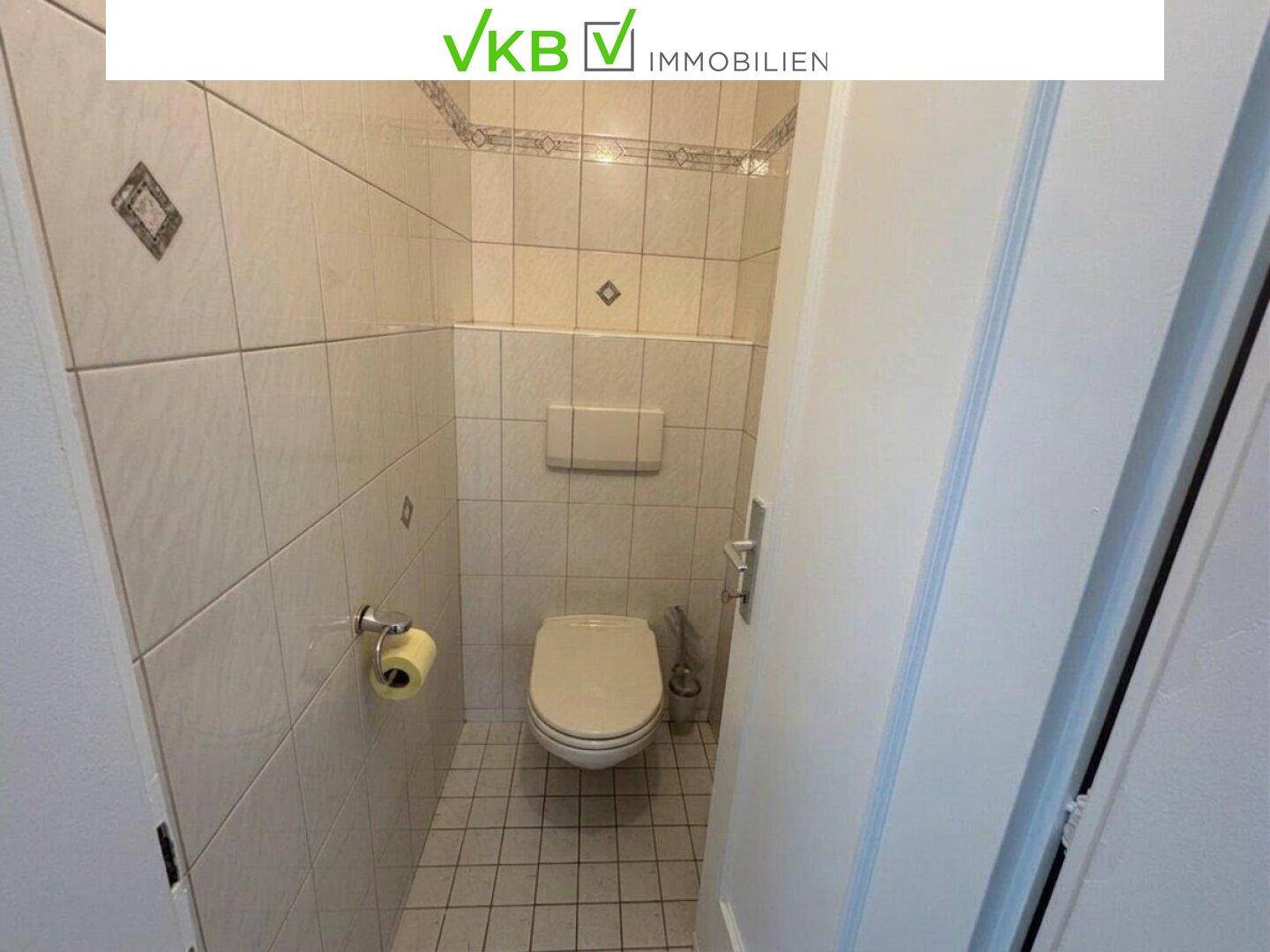 Separate Toilette mit hellen Fliesen und wandmontiertem WC, sauber und funktional.