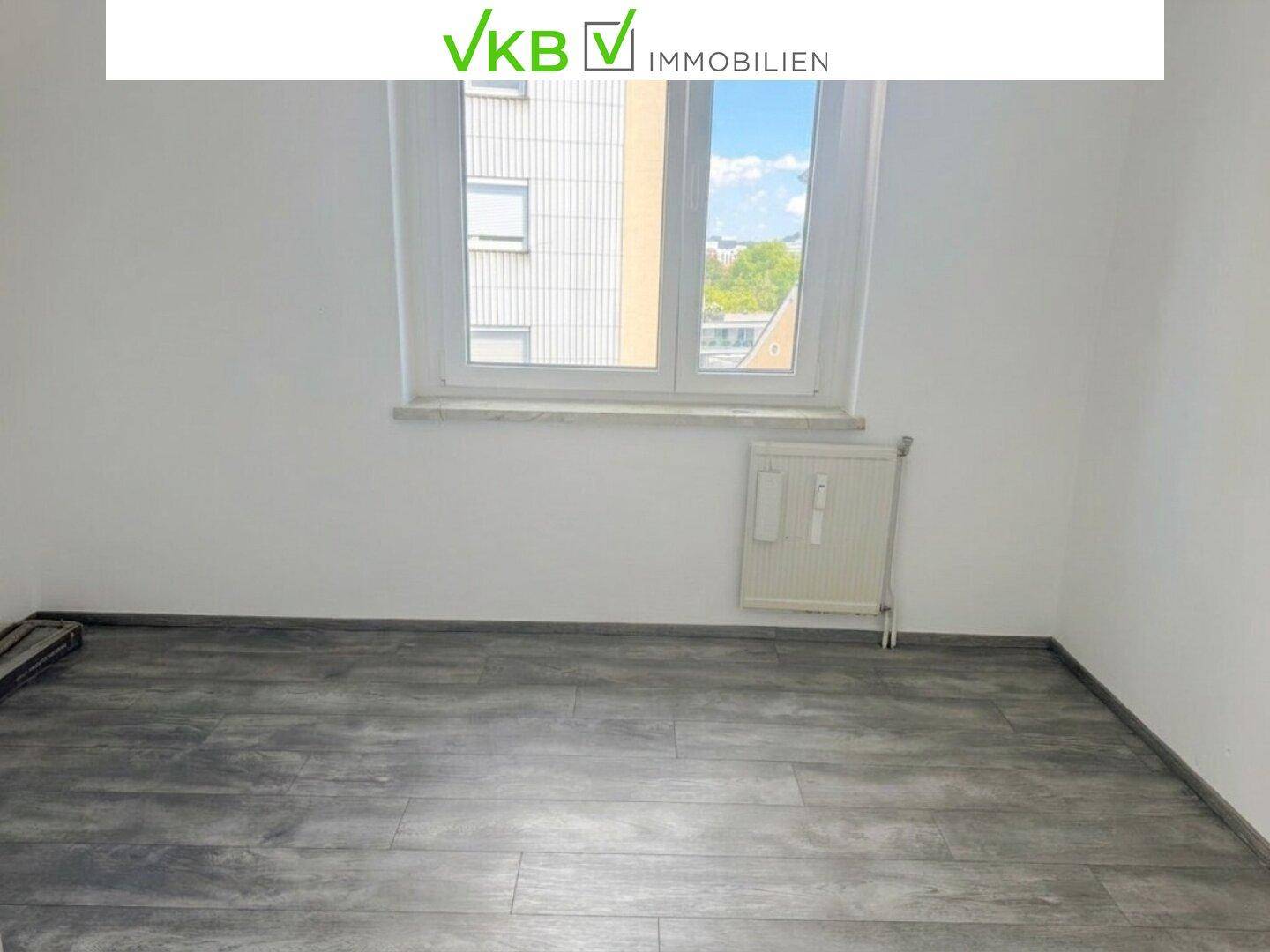 Leeres Schlafzimmer mit grauem Laminatboden und großem Fenster, ideal für individuelle Gestaltung.